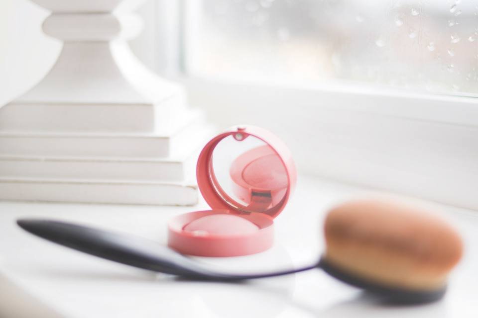 A pink blush compact with a makeup brush