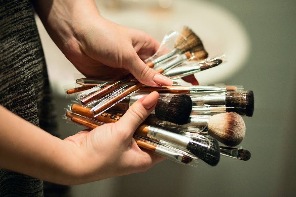 Hands holding a bunch of makeup brushes