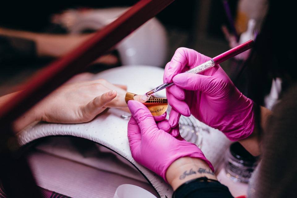 A manicurist painting nails with pink gloves