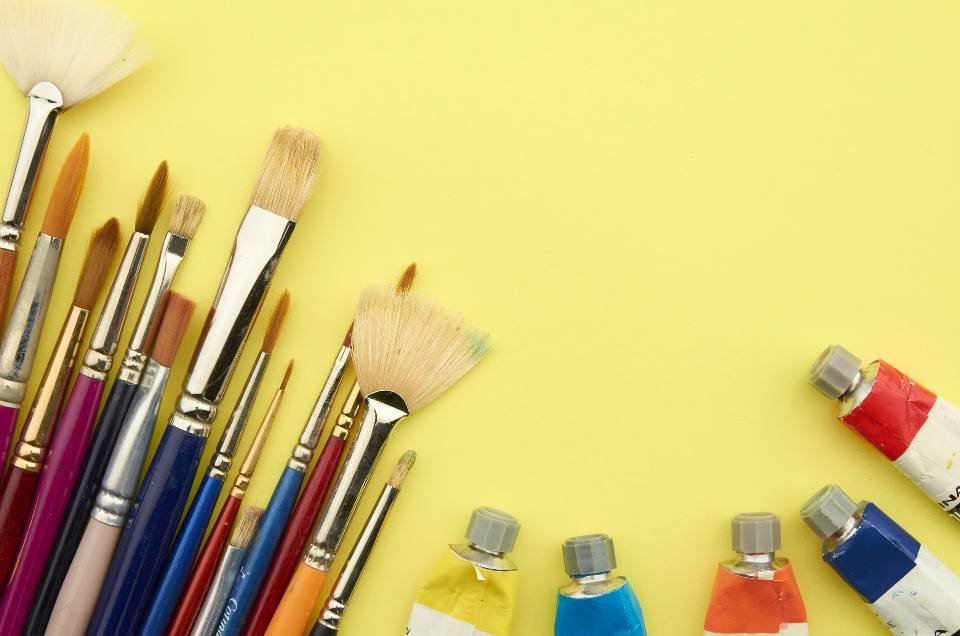 Paintbrushes and paint tubes on a yellow background