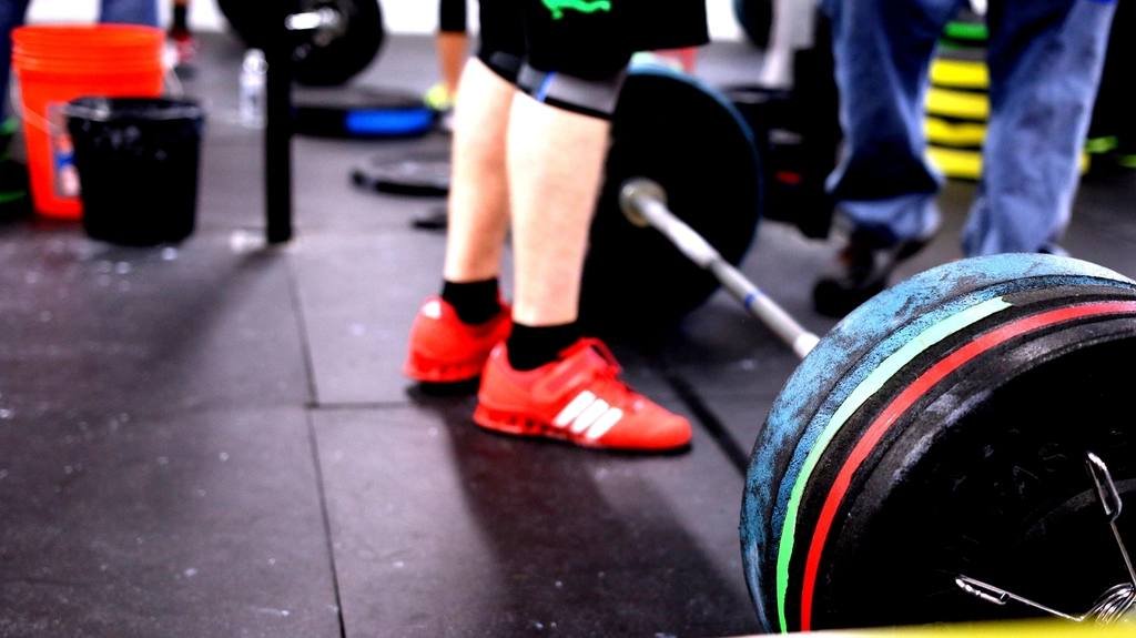 A lifter's red shoes beside a loaded barbell