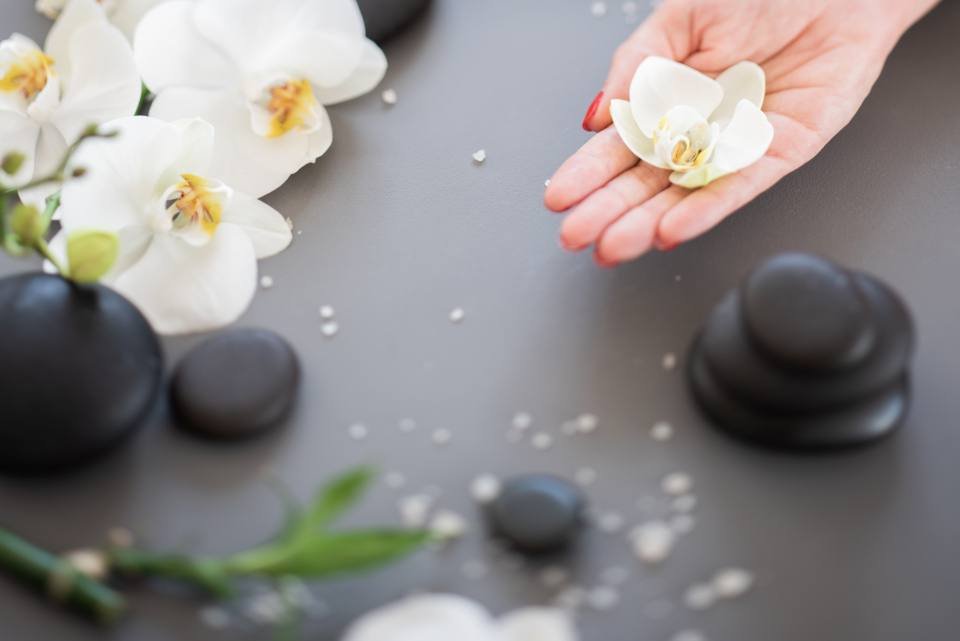 A hand holding a white orchid above spa stones
